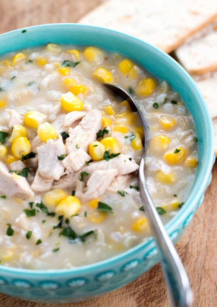 A bowl of chicken and rice corn chowder with a spoon in it