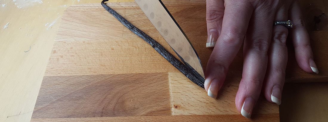 a vanilla bean pod being scraped with a knife