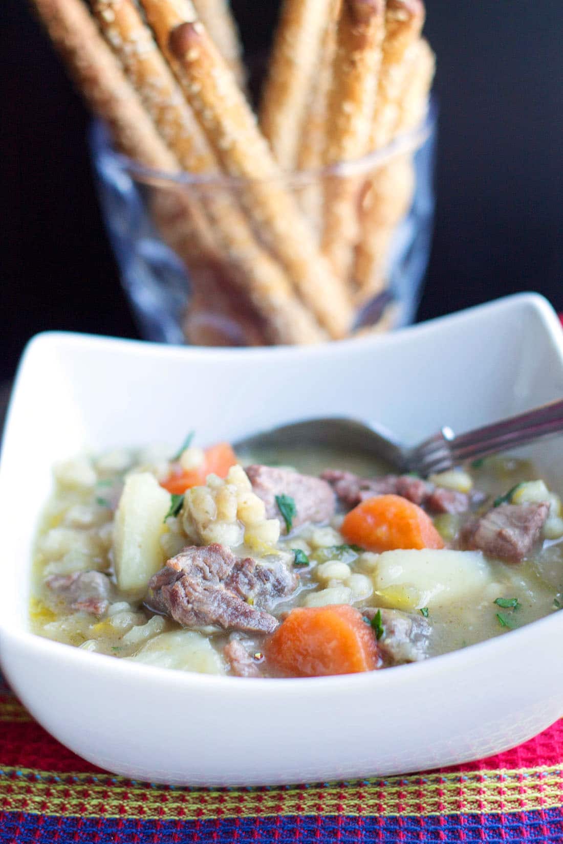 Irish Stew in a bowl with a spoon and breadsticks in the background