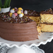 A piece of yellow celebration cake with chocolate frosting being removed from the whole cake