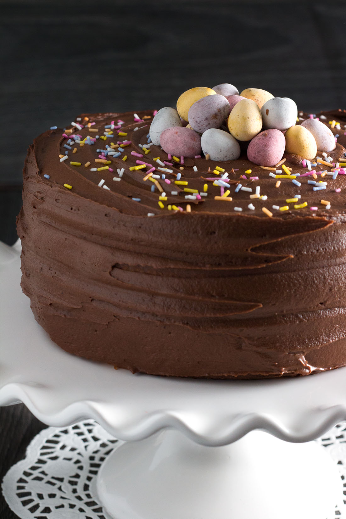 close up of yellow celebration cake with chocolate frosting on a serving dish topped with chocolate eggs and sprinkles