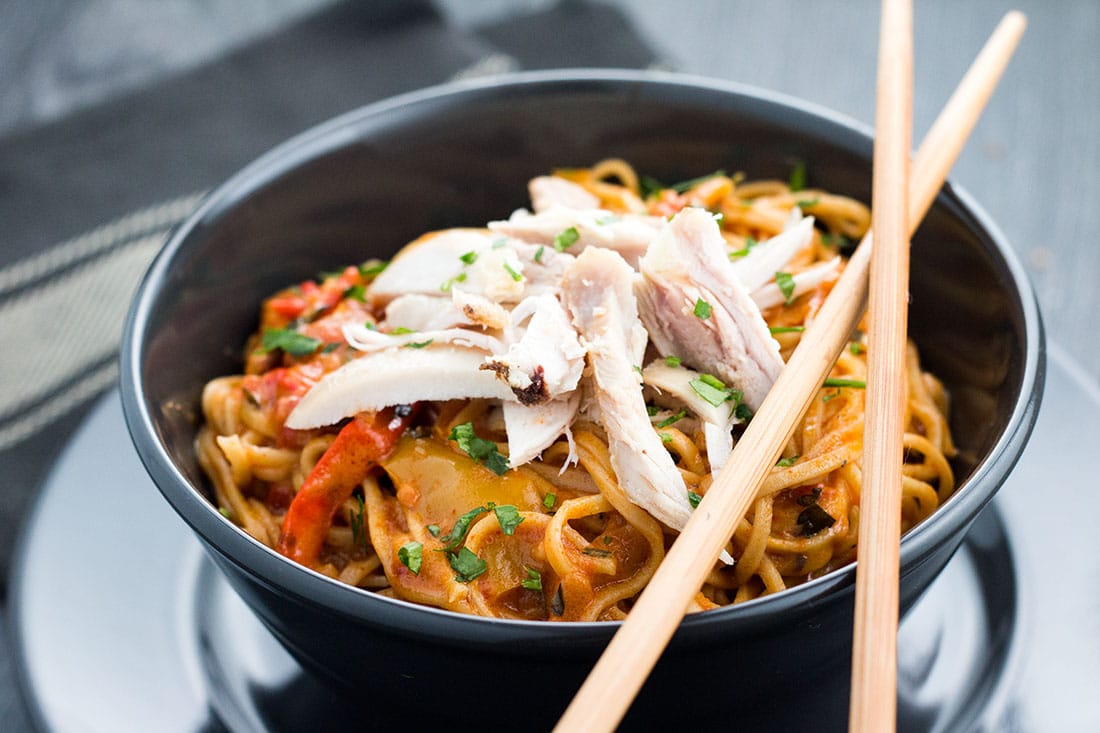 A bowl of Thai curry noodles with chicken with two chopsticks placed on top