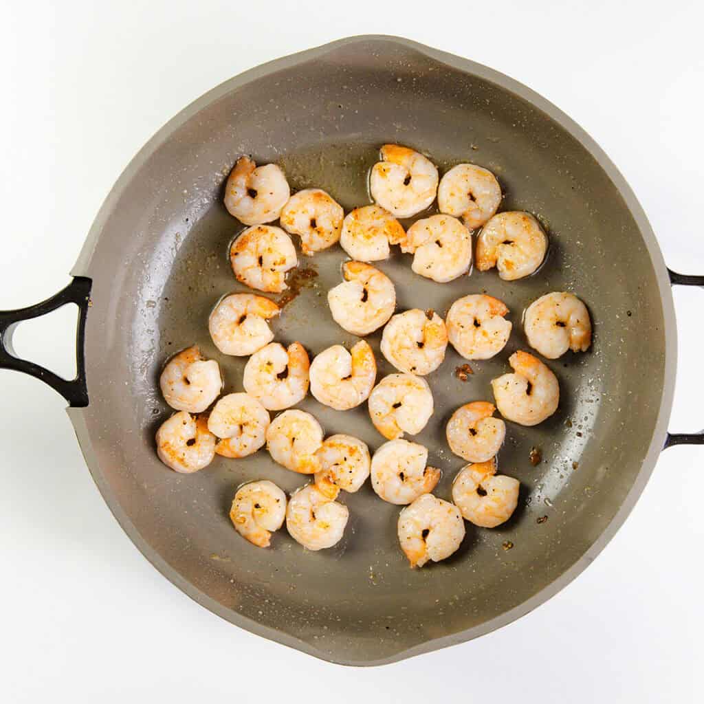 Cooked shrimp are arranged in a single layer in a gray skillet with two handles, seen from above on a white background. Perfectly browned and lightly seasoned, these are ideal for making 10 Minute Cashew Shrimp.