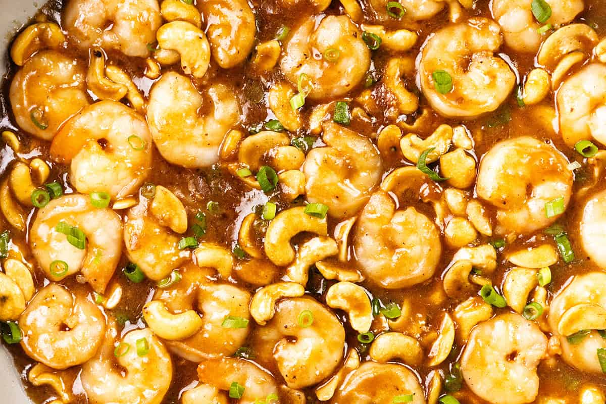 Close-up of a 10 Minute Cashew Shrimp stir-fry in thick brown sauce, garnished with sliced green onions. The dish appears glossy and richly coated, highlighting the shrimp and nuts.