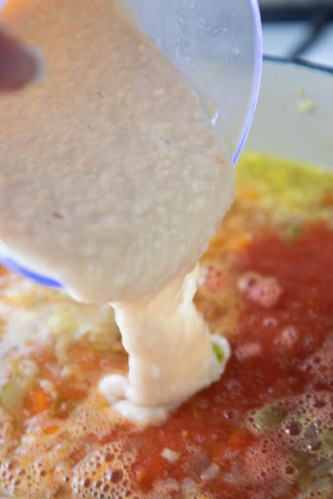 pureed beans being added to the soup mixture