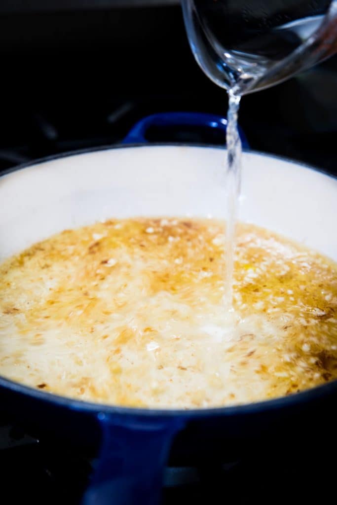 wine being poured into the pan with the garlic