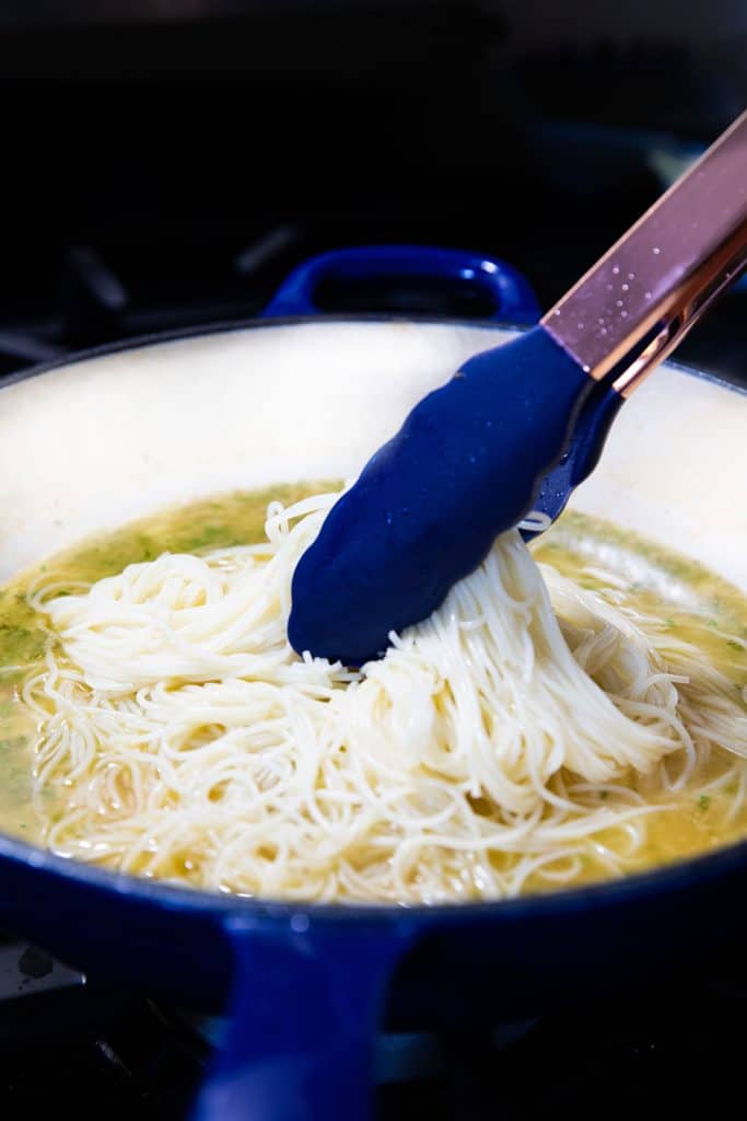 pasta being added to the sauce with tongs
