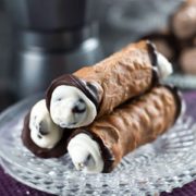 A close up of three cannoli with the ends dipped in dark chocolate with the creamy filling and chocolate chips bulging out of them