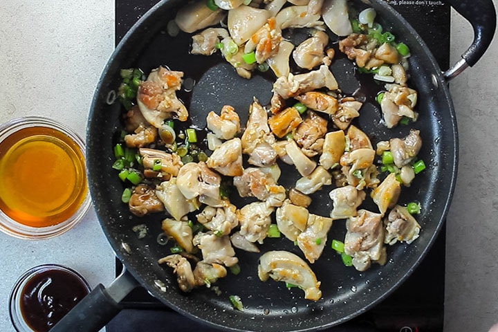 The chicken added to the onions, garlic and green onions in a wok stir frying in oil