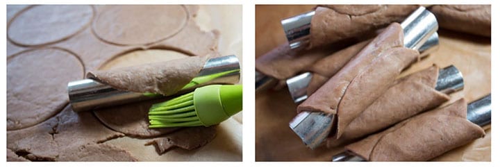 cannoli tubes with the dough rounds wrapped around them and a 2nd with The dough round halfway wrapped around the tube being brushed with egg wash