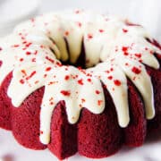 a vibrant colored Red Velvet Bundt Cake drizzled with cream cheese frosting with cake crumbs as decoration