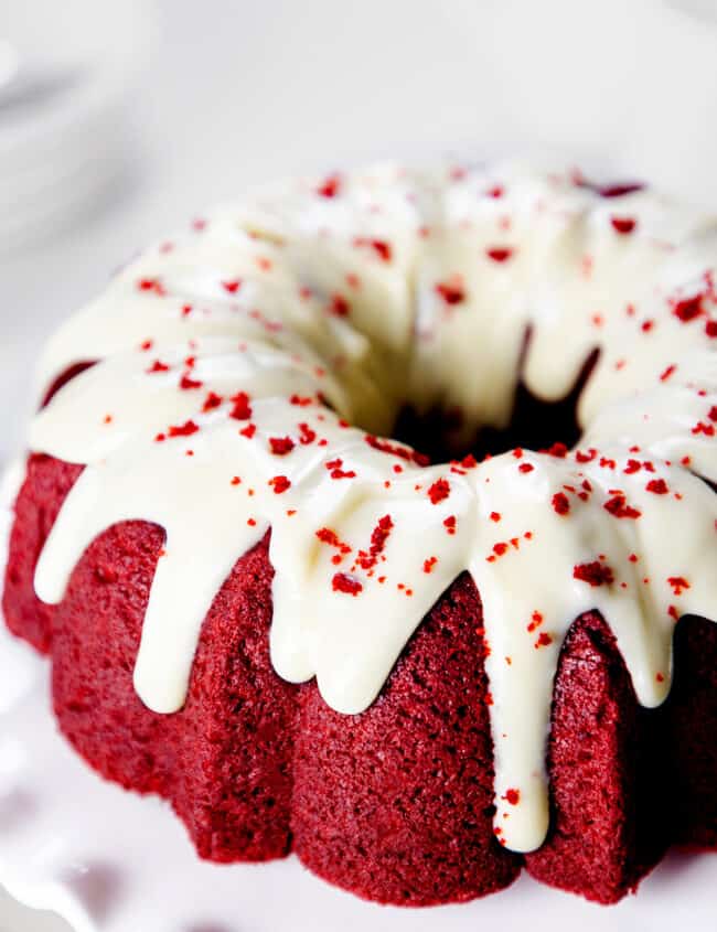 A close up image of a vibrant Red Velvet Bundt Cake with Cream Cheese Icing decorated with red cake crumbs