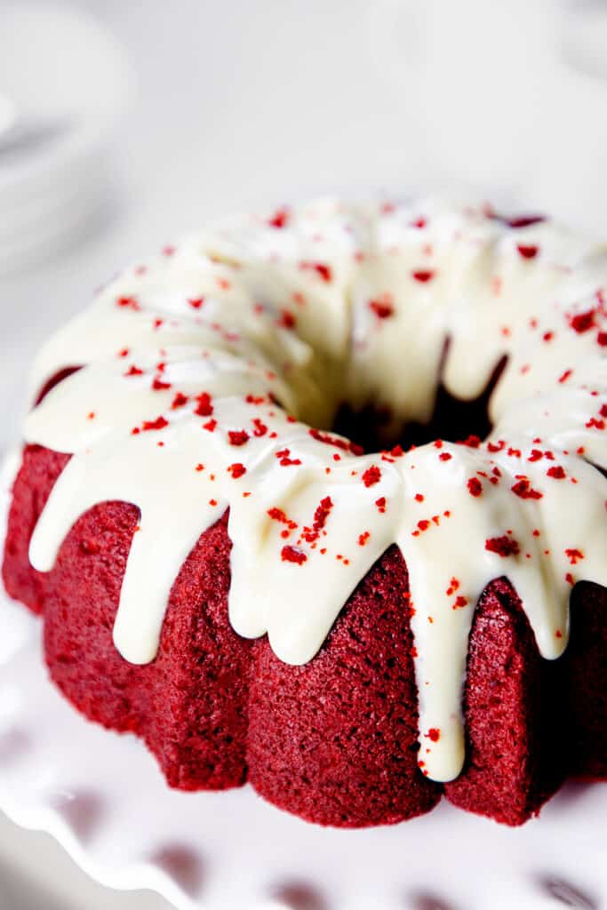 A close up image of a vibrant Red Velvet Bundt Cake with Cream Cheese Icing decorated with red cake crumbs