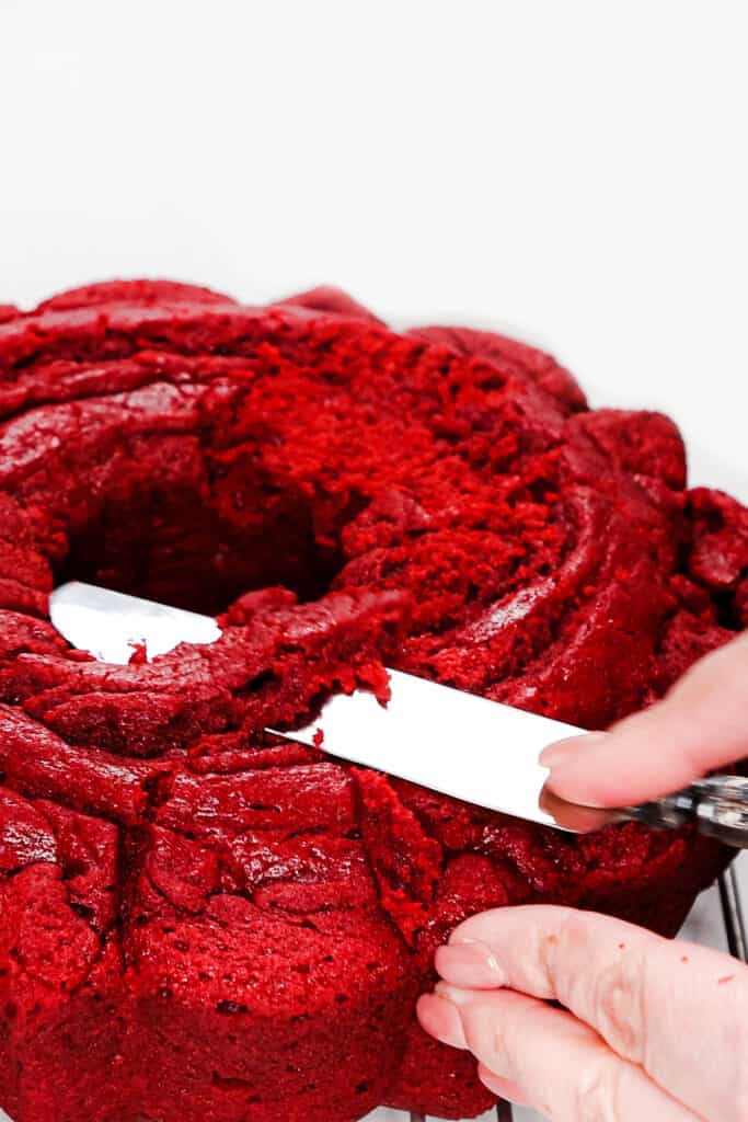 a knife slicing a small piece of cake off the surface of a Red Velvet Bundt Cake