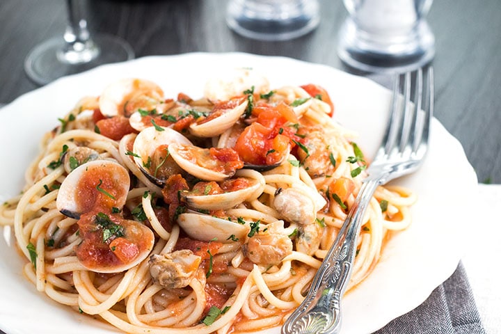 A plate full of Spaghetti with Red Clam Sauce with the clams still in their shells. 