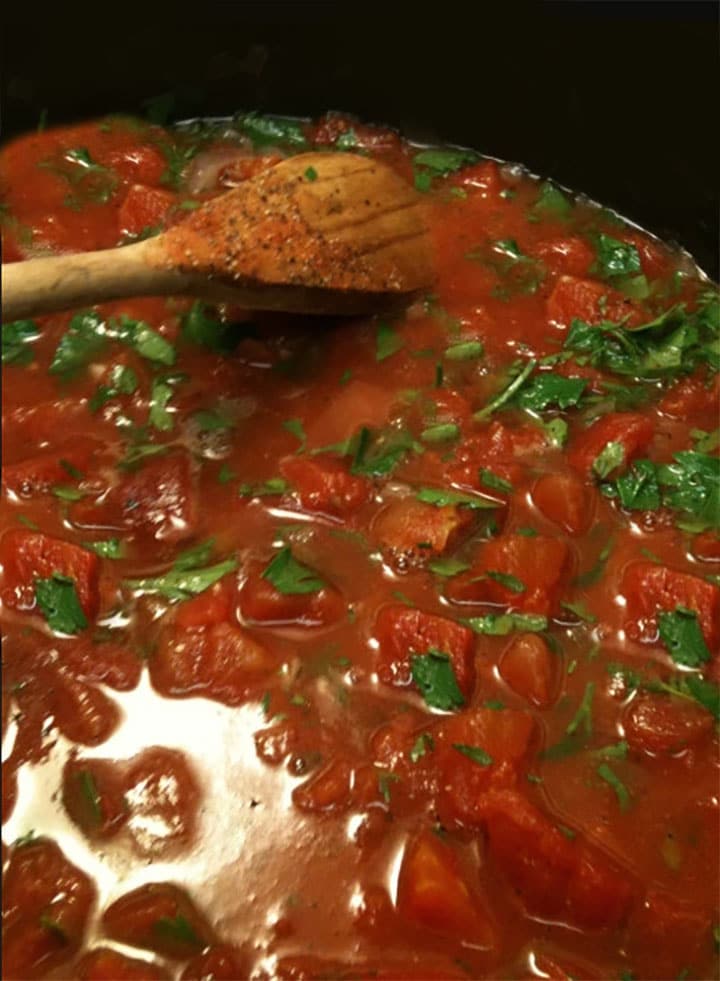 A pan with the tomatoes white wine and parsley being mixed together with a wooden spoon