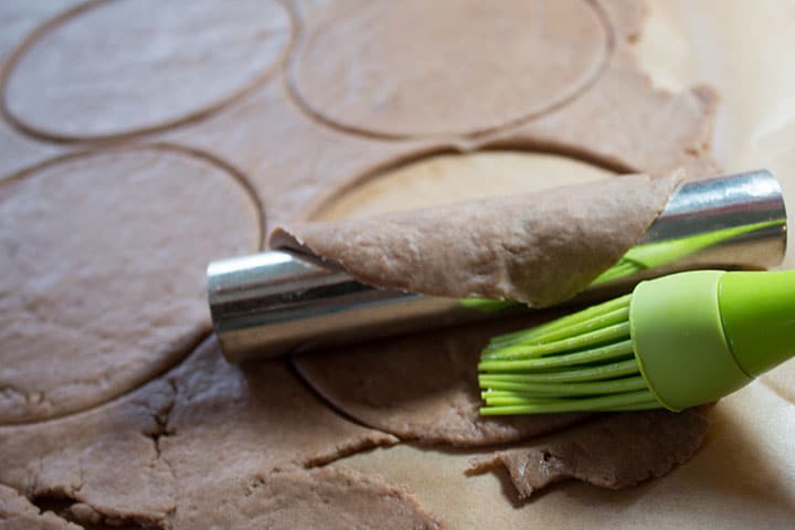 The dough round halfway wrapped around the tube being brushed with egg wash