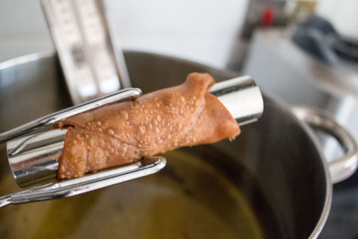 A p[air of tongs removing the cannoli shell from the oil