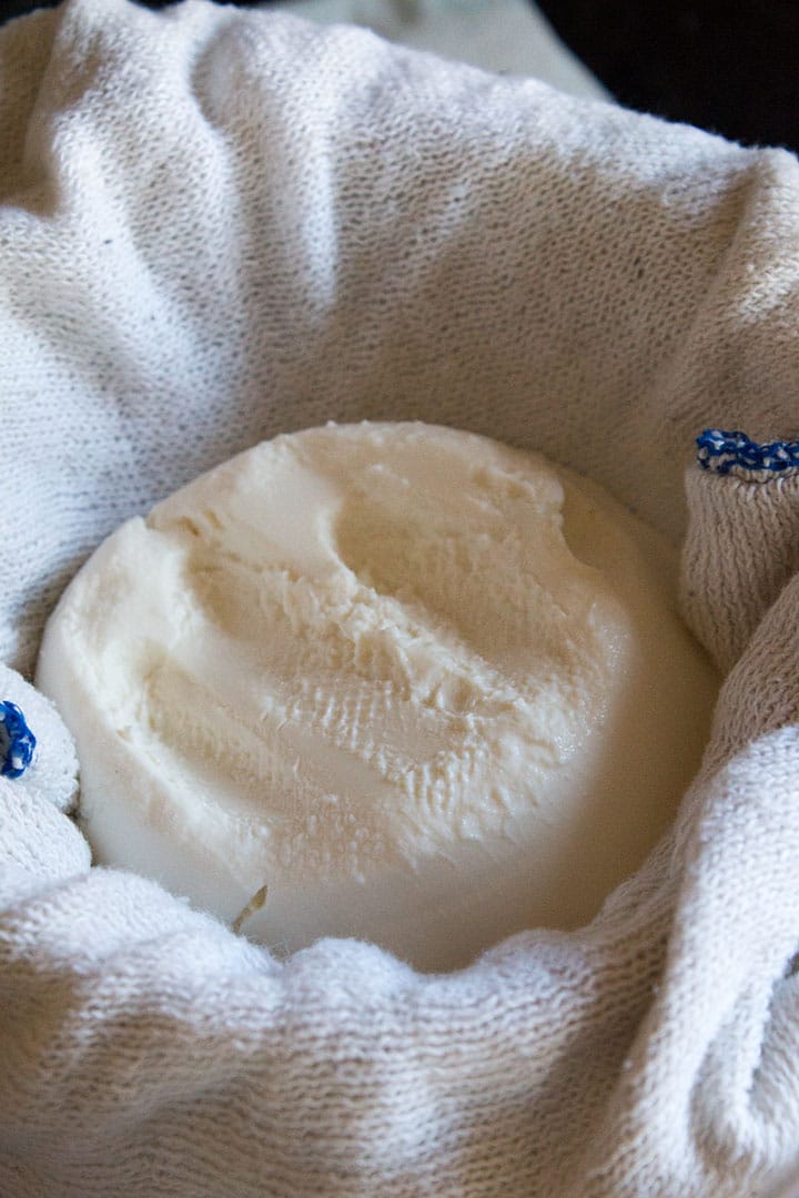 A close up of ricotta cheese in a strainer lined with a cloth