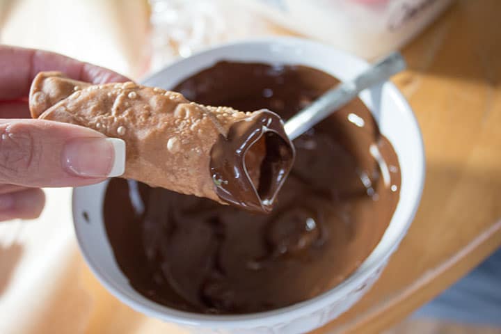 A close up of a cannoli shell with one end dipped in melted chocolate
