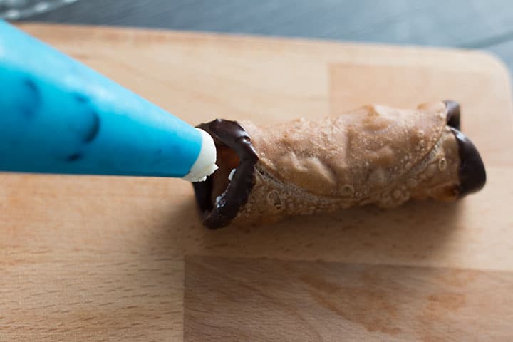 A close up of a piping bag filled with cannoli filling going to pipe a cannoli shell