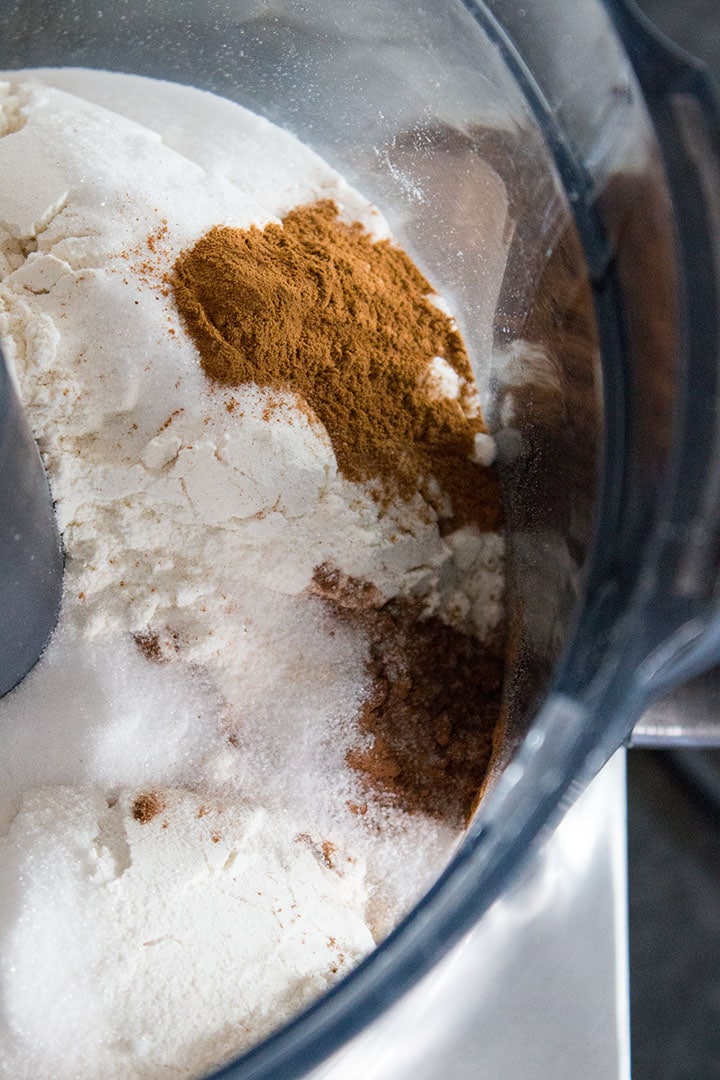 A close up of a food processor bowl with flour covered with other dry ingredients that haven't been mixed in