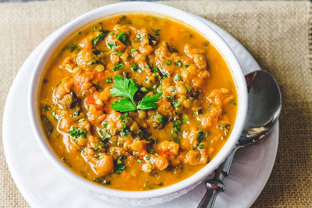 a close up of a big bowl of lentil soup garnished with parsley