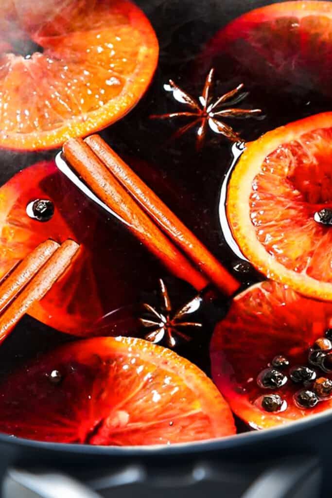 Cranberry Holiday Cocktail cooking in a pot with cinnamon, star anise, orange slices, and juniper berries