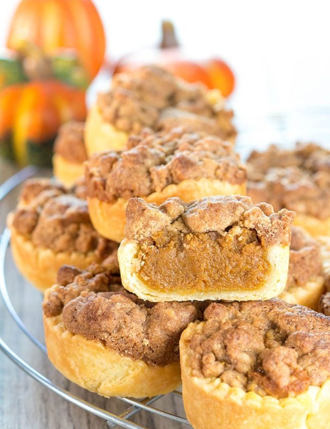 mini pumpkin pies stacked on a cooling rack with one cut open to show the filling