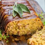 Bacon Wrapped Sausage Stuffing with a slice cut out of it showing the stuffing with sausage meat throughout