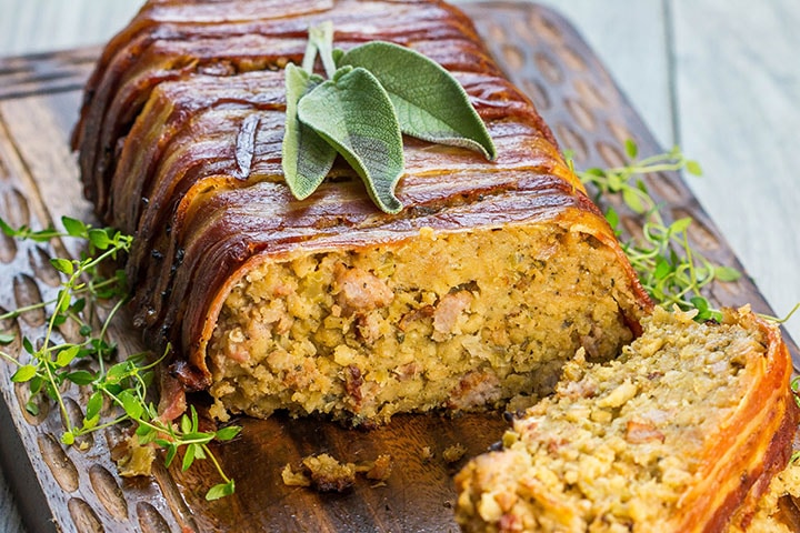 Bacon Wrapped Sausage Stuffing with a slice cut out of it showing the stuffing with sausage meat throughout
