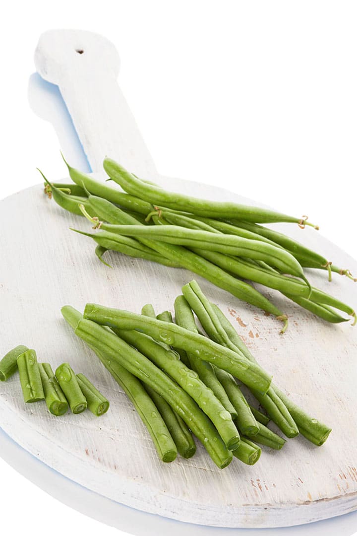 fresh green beans on a chopping board with some trimmed on the ends
