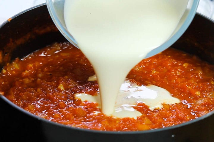 The cream pouring into the pan with the tomato sauce