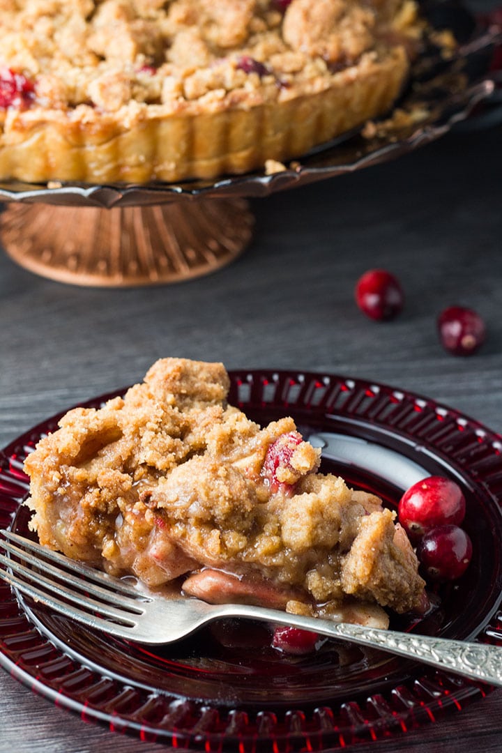 A slice of apple cranberry crumb pie on a red glass plate with a fork next to it