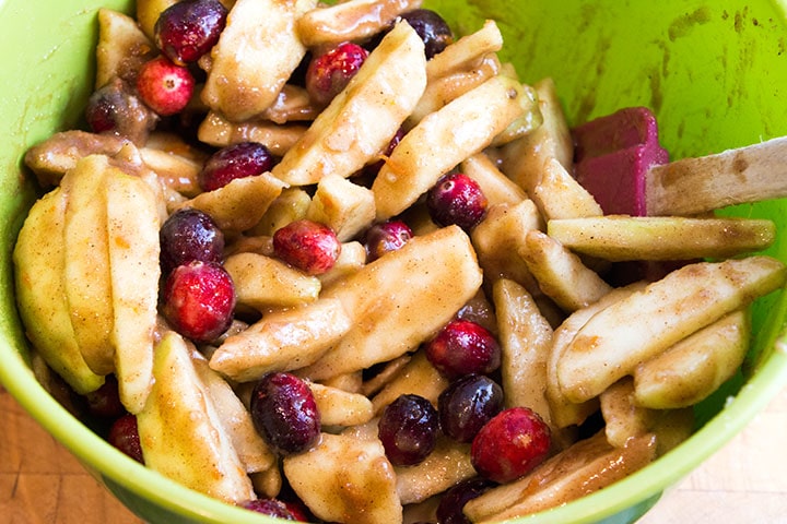 A bowl with sliced apples and cranberries coated in the sugar and spices