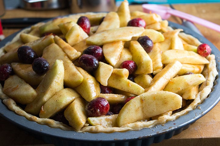 A pie pan filled with apples and cranberries coated in a cinnamon spice and sugar mixture
