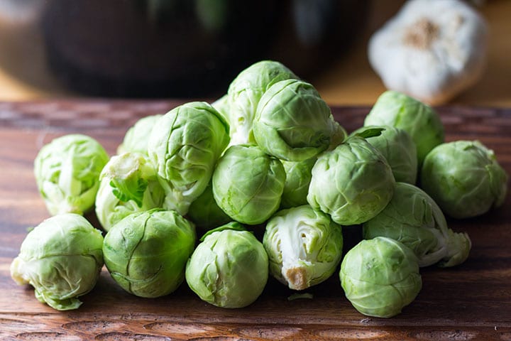 A cutting board with a pile of cleaned brussel sprouts.