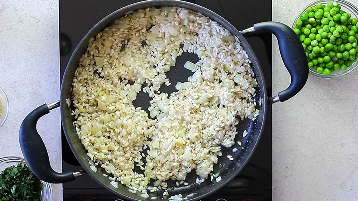 The rice in the pan with the cooked onions, celery and garlic