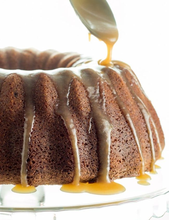 A Brown Sugar Bundt Cake on a glass cake stand being drizzled with Caramel Glaze