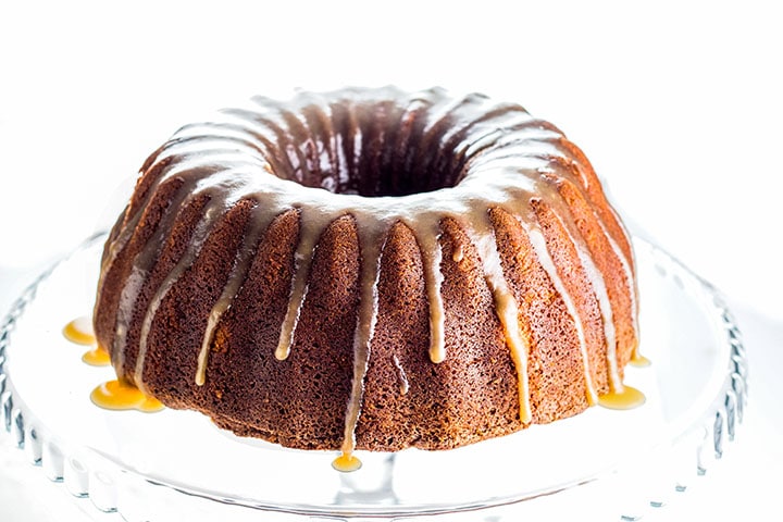 A Brown Sugar Bundt Cake on a glass cake stand dripping with Caramel Glaze
