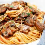 A close up image of plate with a serving of spaghetti topped with a tomato mushroom sauce.