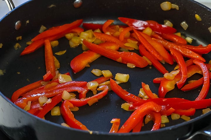 The sliced pepper and onion cooking in the pan