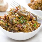 Easy Mushroom & Bacon Risotto in a white bowl scattered with fresh herbs