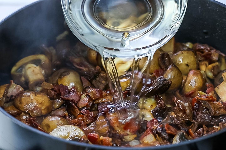 The vermouth being poured into the pan with the mushroom mixture.