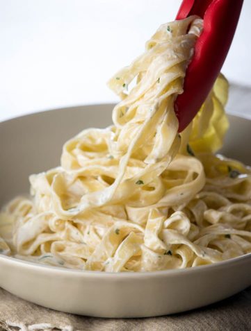 The Best Fettuccine Alfredo of Your Life being served with tongs