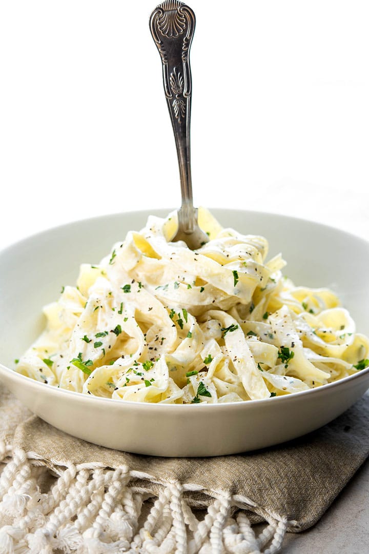 Fettuccine with Alfredo sauce in a bowl sprinkled with parsley being twirled with a fork