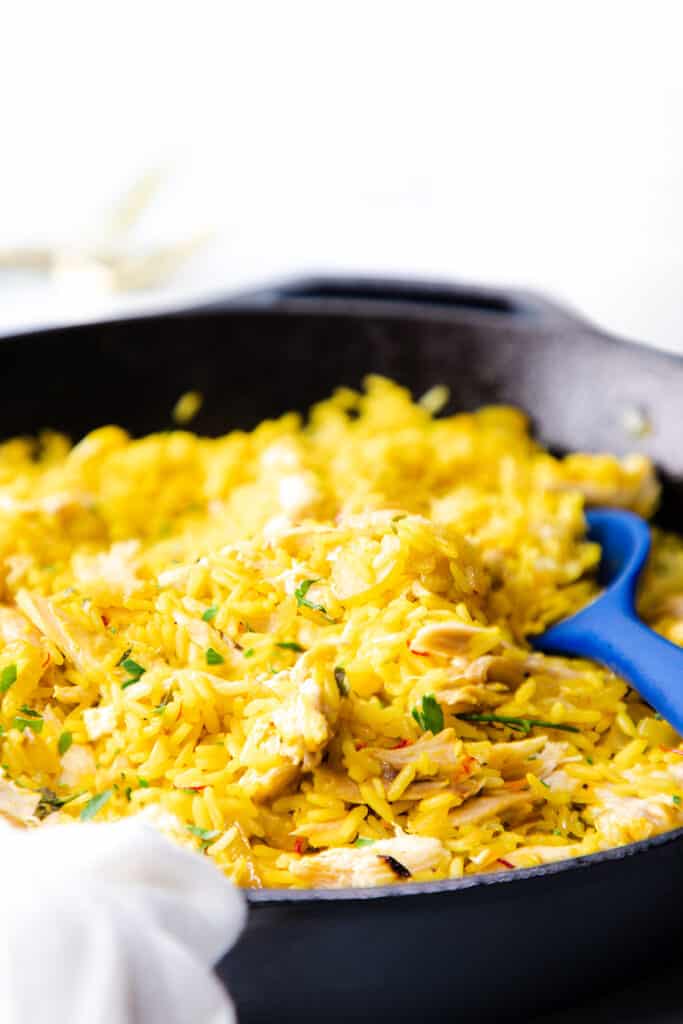 chicken and yellow rice in a pan with a blue spoon