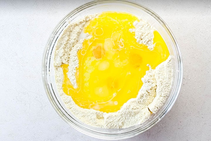 The eggs, milk, butter, and oil added to the dry ingredients in a bowl 