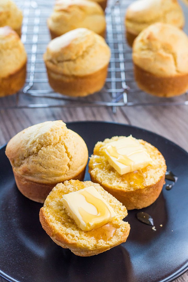 A plate of corn muffins with one cut in half with butter and honey drizzled over it