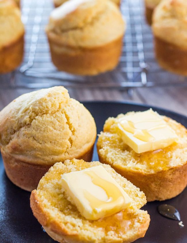A corn muffin on a plate with butter and honey on it
